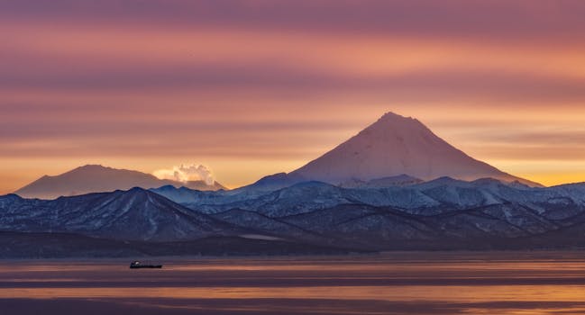 A tranquil sunrise view of snowy mountains and a calm body of water.
