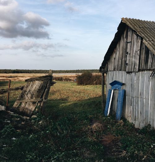 Free Weathered barn with broken fence, lush greenery, and cloudy sky in rural setting. Stock Photo