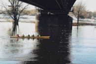 冬季的河面上，四人赛艇队在桥下练习，倒影随波荡漾