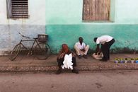 Men sitting on a sidewalk next to a bicycle, selling goods. Urban street scene.