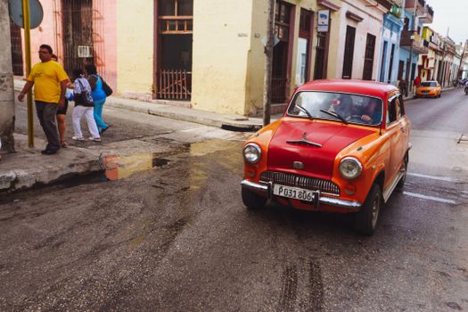 Classic vintage car drives down a colorful street in Havana, Cuba.