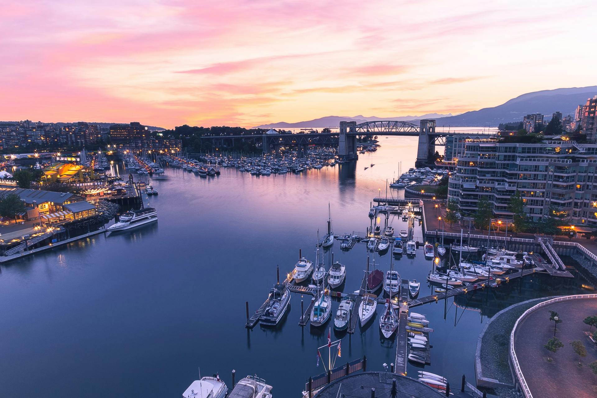 Sweeping view of Vancouver's harbor and skyline at twilight, featuring boats and Burrard Bridge.
