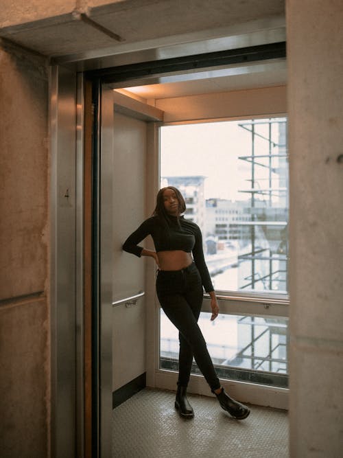 A Woman in Black Tank Top and Black Pants Standing Beside Glass Window