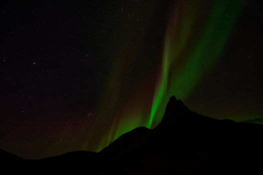 Breathtaking view of the Northern Lights illuminating a mountain silhouette under a starry night sky.