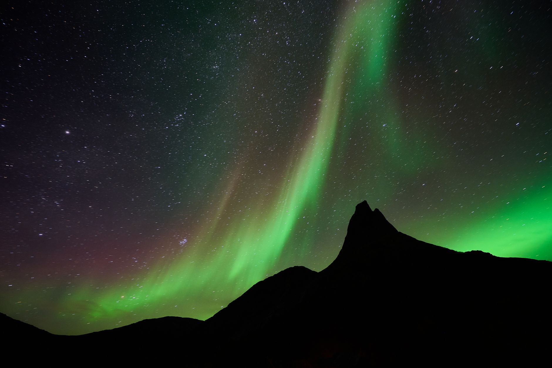 A mesmerizing display of northern lights dancing over a mountainous silhouette and starry night sky.