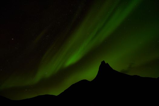 Stunning view of the aurora borealis dancing over mountain peak at night.