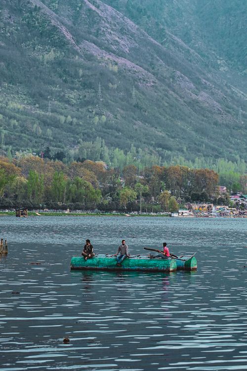 Free Three adults on a green raft enjoying a serene lake surrounded by mountains. Stock Photo