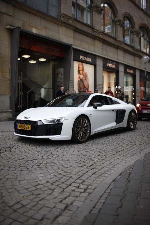 Free White Audi R8 parked on cobblestone street in front of retail stores. Stock Photo