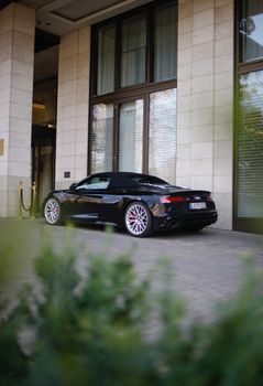 Black luxury convertible sports car parked outside a modern building on a clear day.