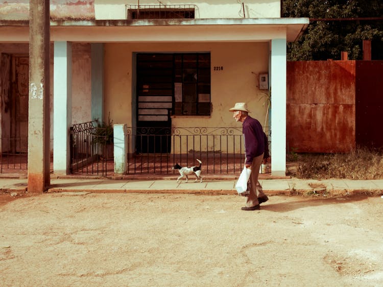 An Elderly Man Walking On The Street With His Dog