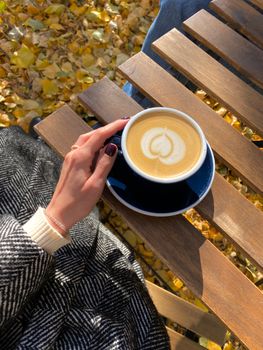 Cozy autumn day with a latte in hand on a wooden table covered in yellow leaves.