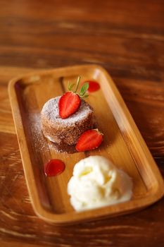 A tempting dessert featuring chocolate cake, strawberries, and ice cream on a wooden tray.