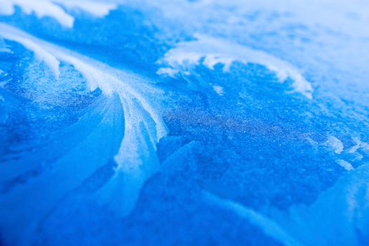 Explore intricate frost patterns on a vivid blue ice surface, capturing winter's natural artistry.