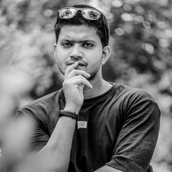 Black and white portrait of a thoughtful young man wearing sunglasses and a t-shirt outdoors.