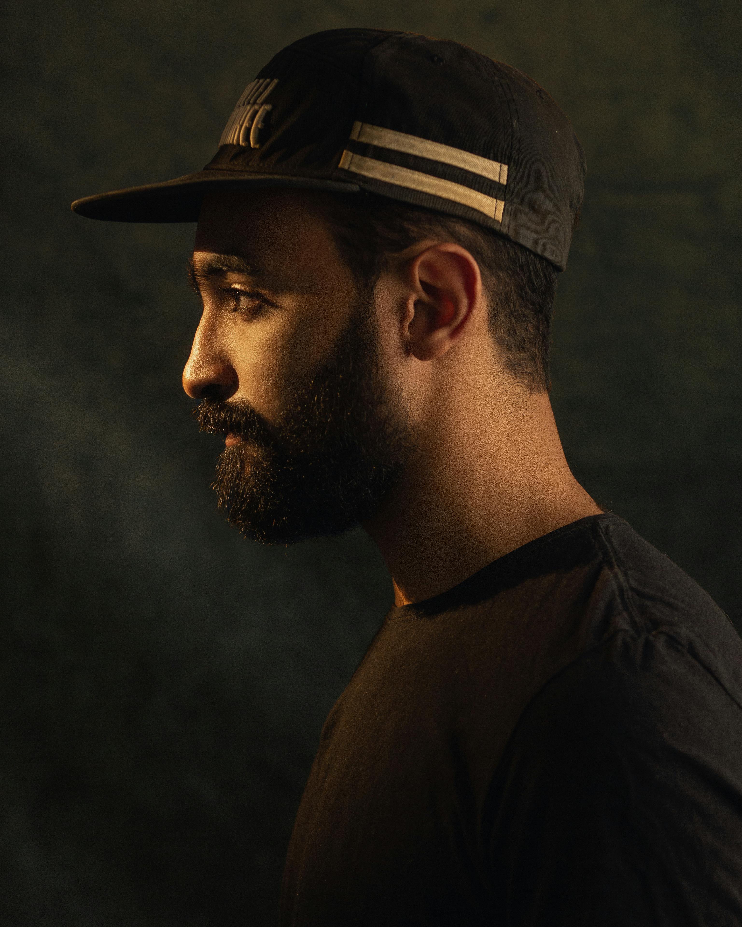 Side view portrait of a bearded man wearing a cap against a dark background.