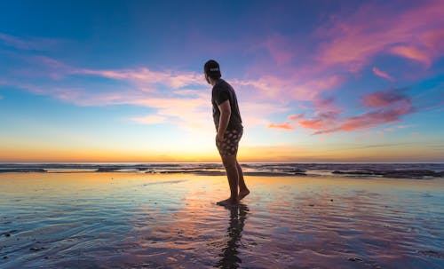 Homme En T Shirt Noir Portant Une Casquette Près Du Plan D'eau Pendant Le Coucher Du Soleil