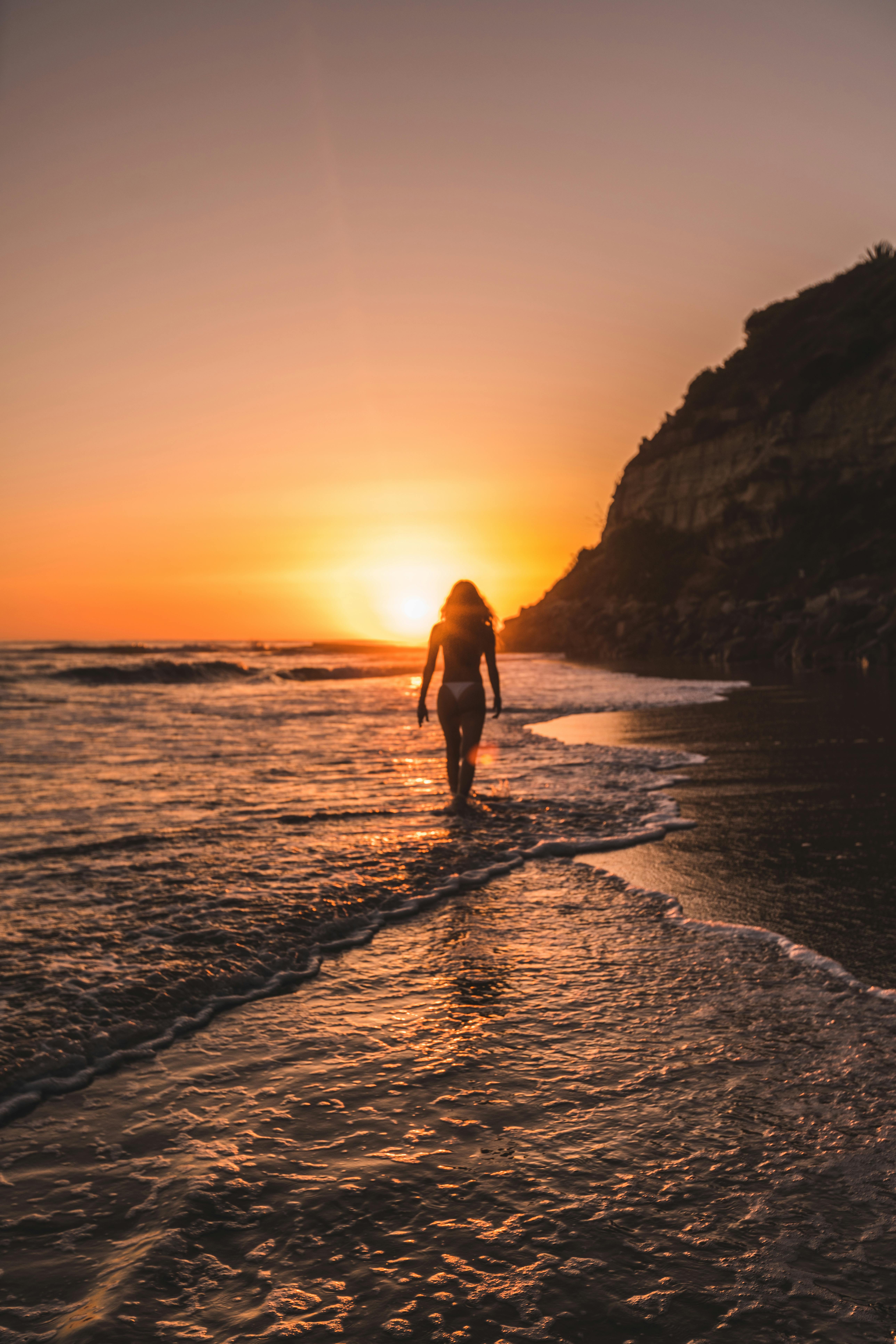 woman in bikini on body of water behind mountain during golden hour