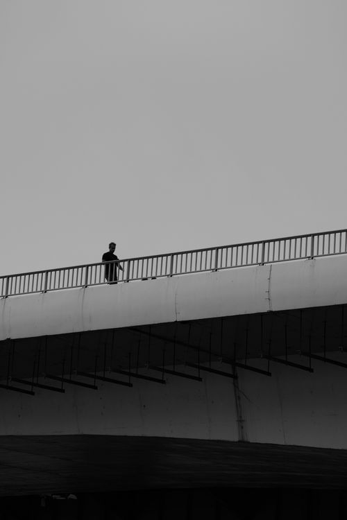 Free A solitary figure silhouetted against a moody sky on an urban bridge. Stock Photo