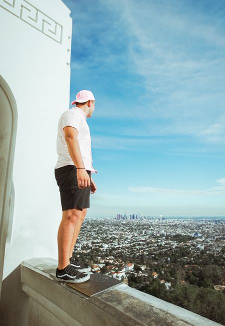 A person stands atop Griffith Observatory, gazing at the expansive Los Angeles skyline under a clear sky.