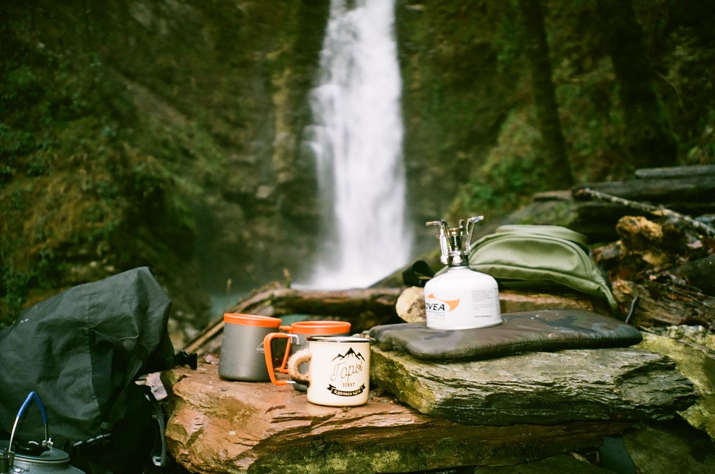 Camping equipment arranged beside a remote forest waterfall