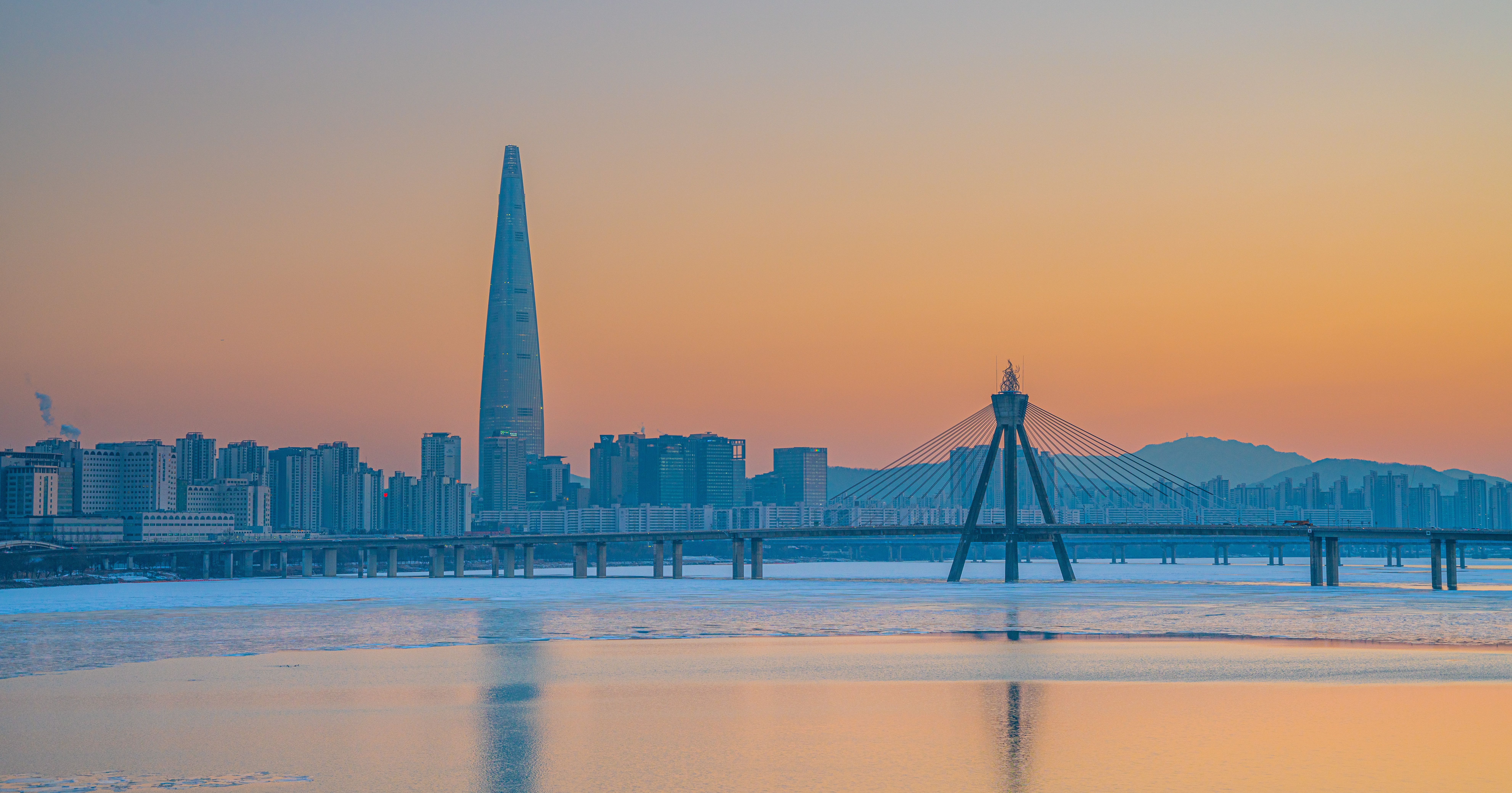Stunning sunset view of Lotte World Tower and Olympic Bridge in Seoul with vibrant sky.