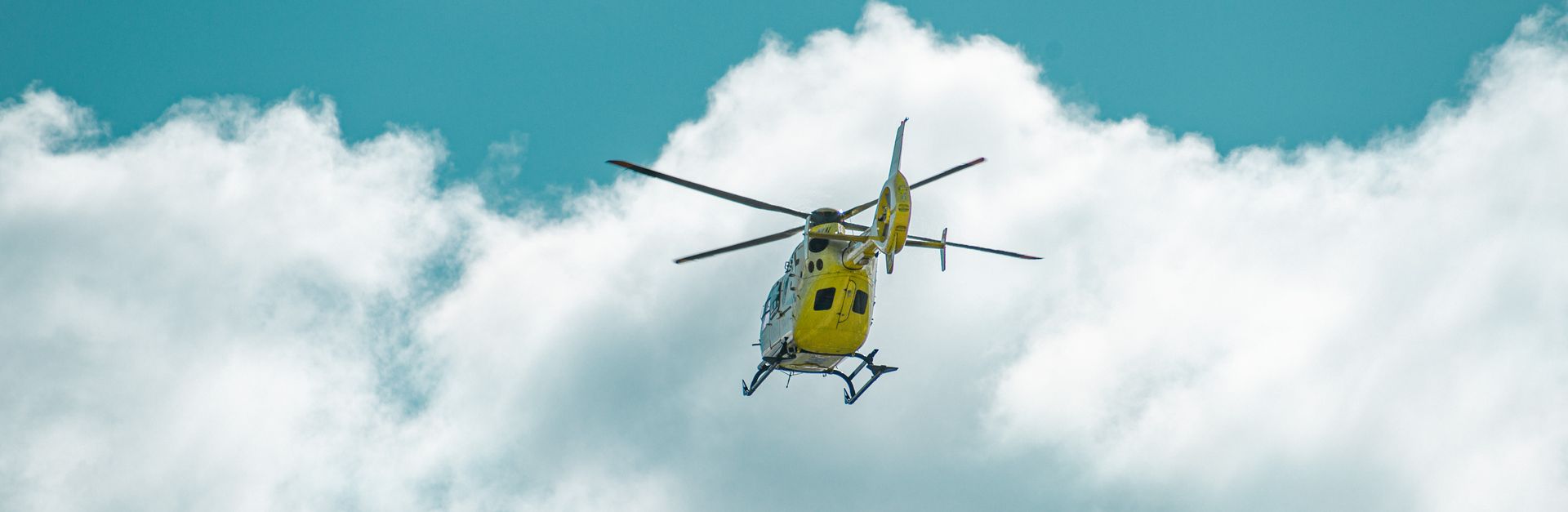 A yellow helicopter flying through white clouds against a blue sky, captured in La Coruña, Spain.