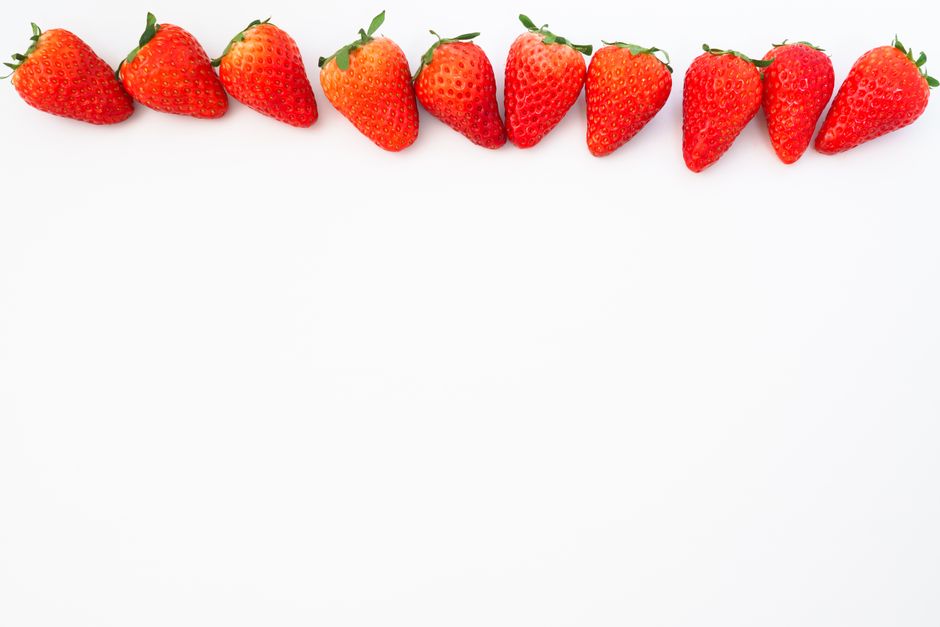 A row of ripe strawberries arranged on a white background, highlighting their vibrant red color.