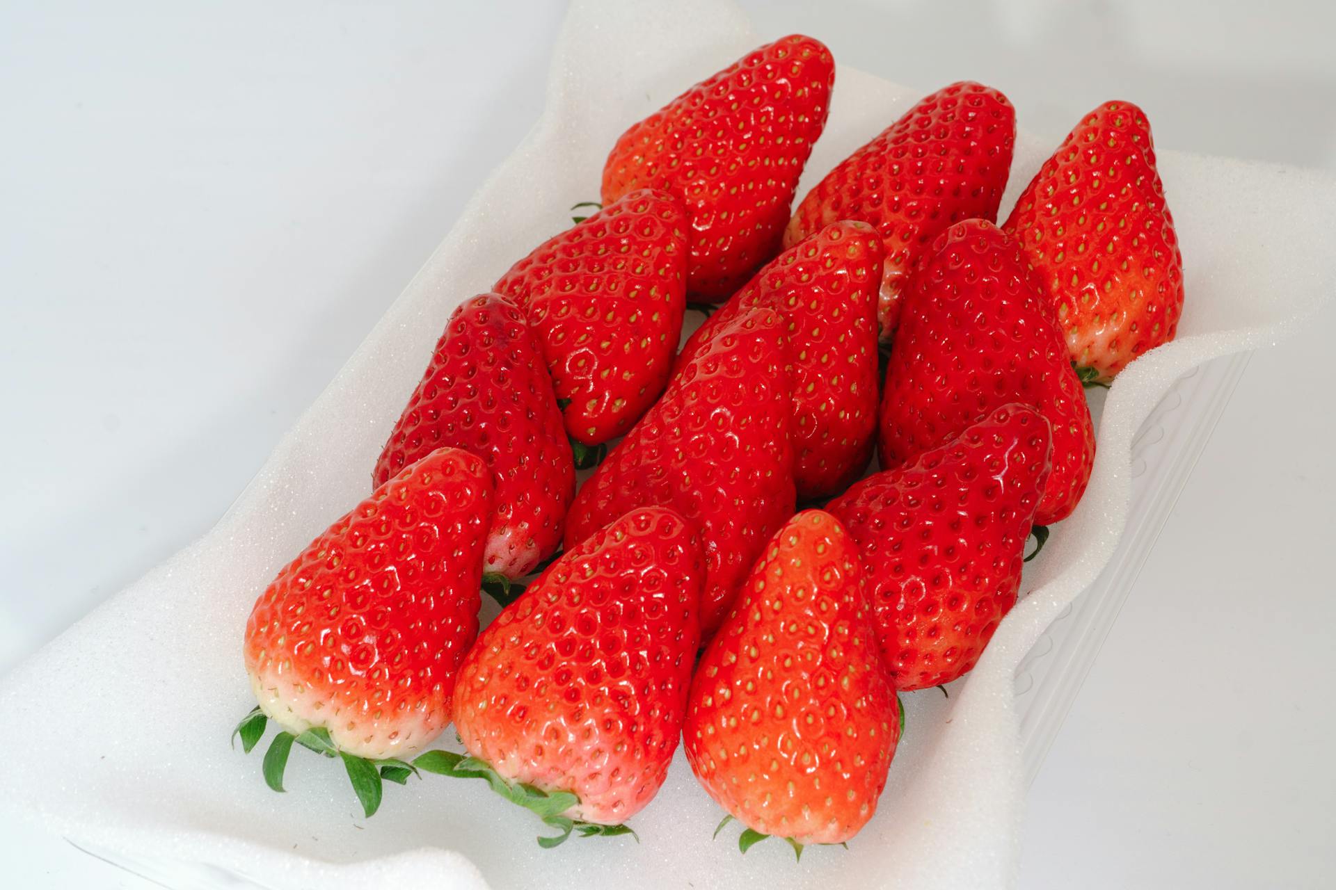 Bright red strawberries arranged neatly on a white foam tray, showcasing freshness and vibrant color.