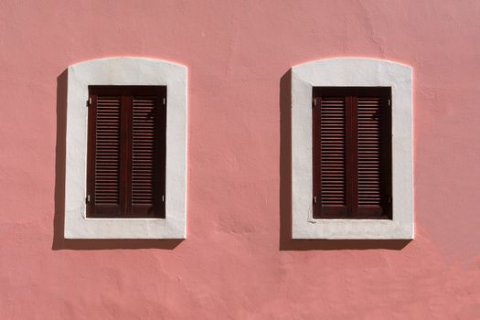 Minimalist architecture featuring a pink facade with two symmetrical wooden shuttered windows.