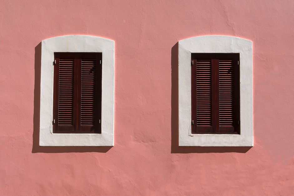 Minimalist architecture featuring a pink facade with two symmetrical wooden shuttered windows.