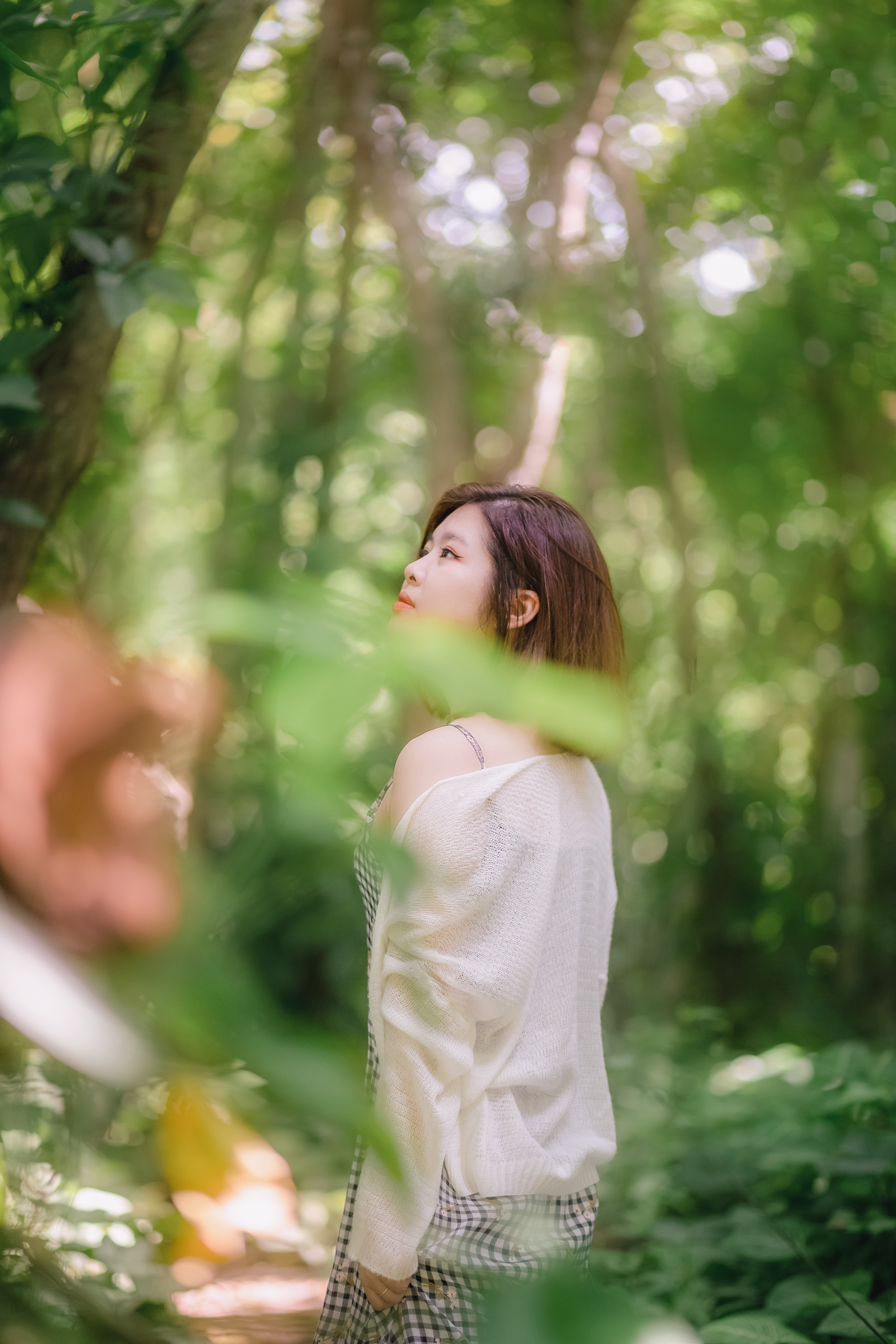 Woman enjoys peaceful moment in a sunlit forest during the day, surrounded by nature.