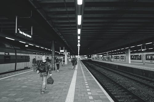 Fotografi Grayscale Dari Pria Yang Membawa Tas Berjalan Di Stasiun Kereta Bawah Tanah
