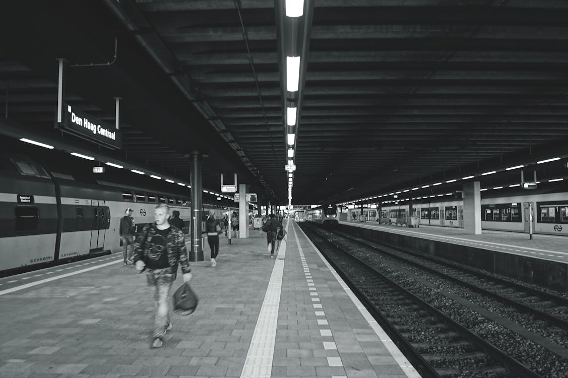 Gratis Fotografi Grayscale Dari Pria Yang Membawa Tas Berjalan Di Stasiun Kereta Bawah Tanah Foto Stok
