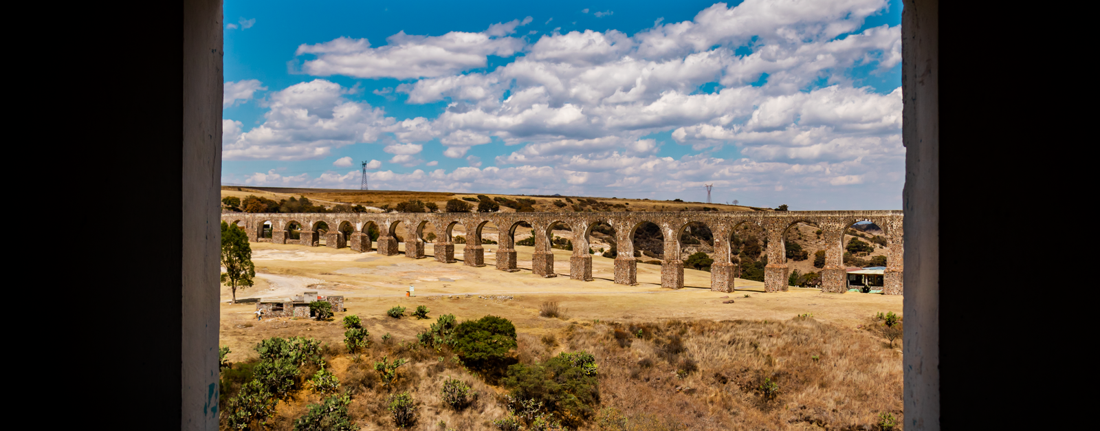 Stunning view of an ancient aqueduct through a window with a vibrant sky, showcasing Mexican history.