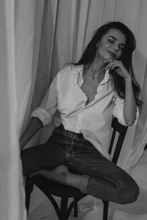 Smiling Woman in a Dress Shirt and Denim Pants Sitting on a Chair