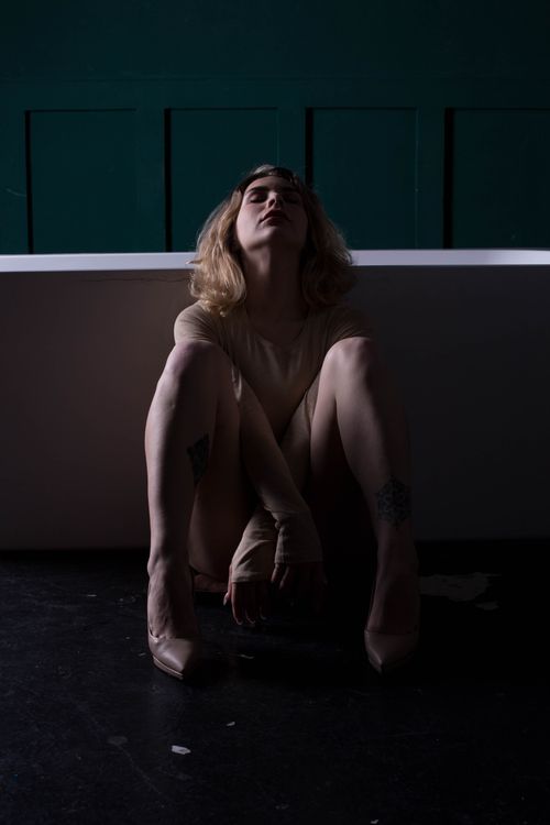 Free Artistic portrait of a woman sitting in a dimly lit studio, eyes closed, creating a moody atmosphere. Stock Photo