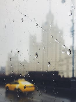 Captivating view through wet window showcasing urban cityscape and yellow taxi on a rainy day.