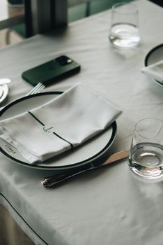 Elegant table setting in a restaurant with white plates, napkins, and glassware in soft lighting.