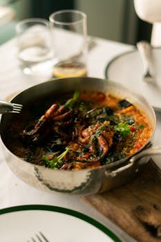 A savory seafood paella dish featuring octopus and fresh vegetables served in a stainless steel pan.