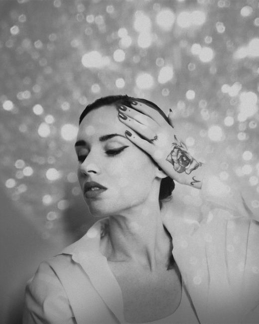 Black and white portrait featuring a tattooed woman posing glamorously, surrounded by bokeh lights.