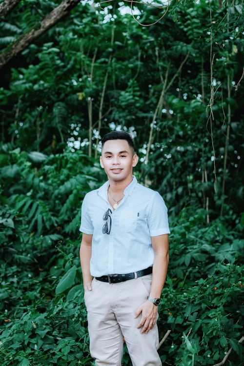 Free A man in a button-down shirt poses confidently in a lush forest setting. Stock Photo