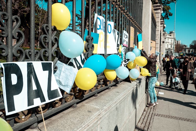 A Man Hanging A Cardboard Sign On A Fence