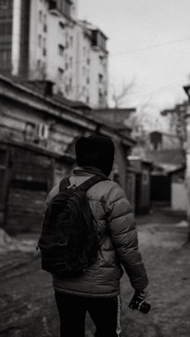 Grayscale Photo Of Person In Winter Jacket Walking And Holding A Camera