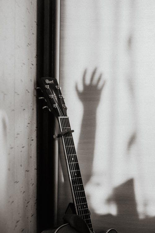 Free A Grayscale of a Guitar and the Shadow of a Person's Hand Stock Photo
