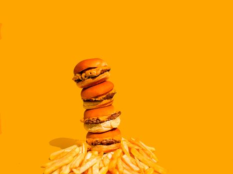 Artistic stack of burgers and fries on a vibrant yellow backdrop, highlighting fast food culture.