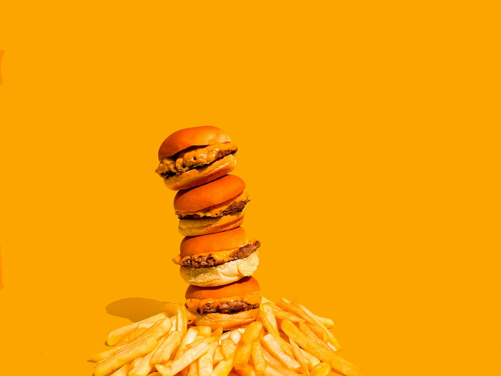 Artistic stack of burgers and fries on a vibrant yellow backdrop, highlighting fast food culture.