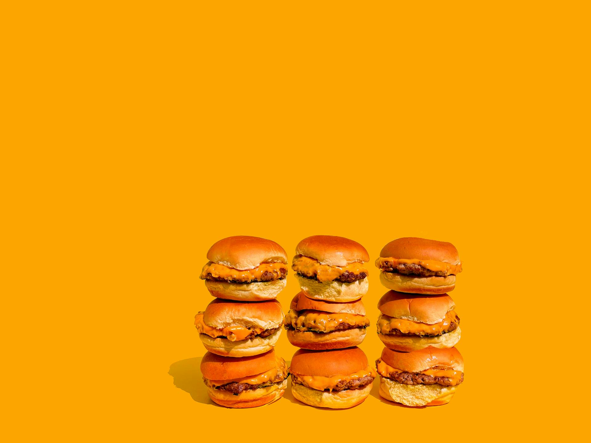 Colorful stack of cheeseburgers against a bright yellow background, ideal for food industry visuals.