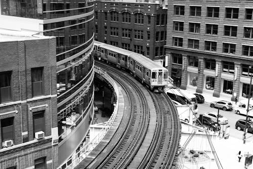 Grayscale Photography of Train on Railroad Near Buildings