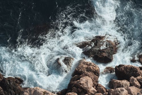 Free A stunning aerial capture of white ocean waves crashing onto rocky formations along the shoreline. Stock Photo