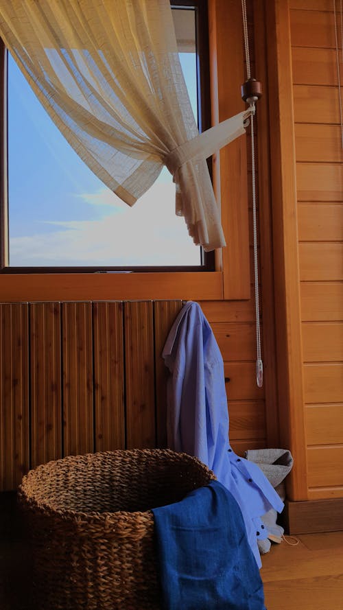 A Glass Window with Wooden Frame and Curtain Near the Woven Basket